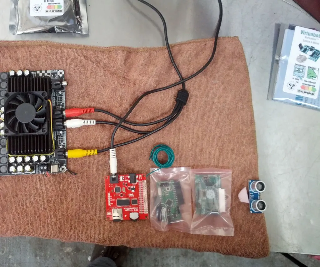 Electronics for the ultrasonic-triggered audio project — an amplifier board, an MP3 trigger board, two Versalino boards in anti-static bags, and an ultrasonic sensor — laid out on a towel.